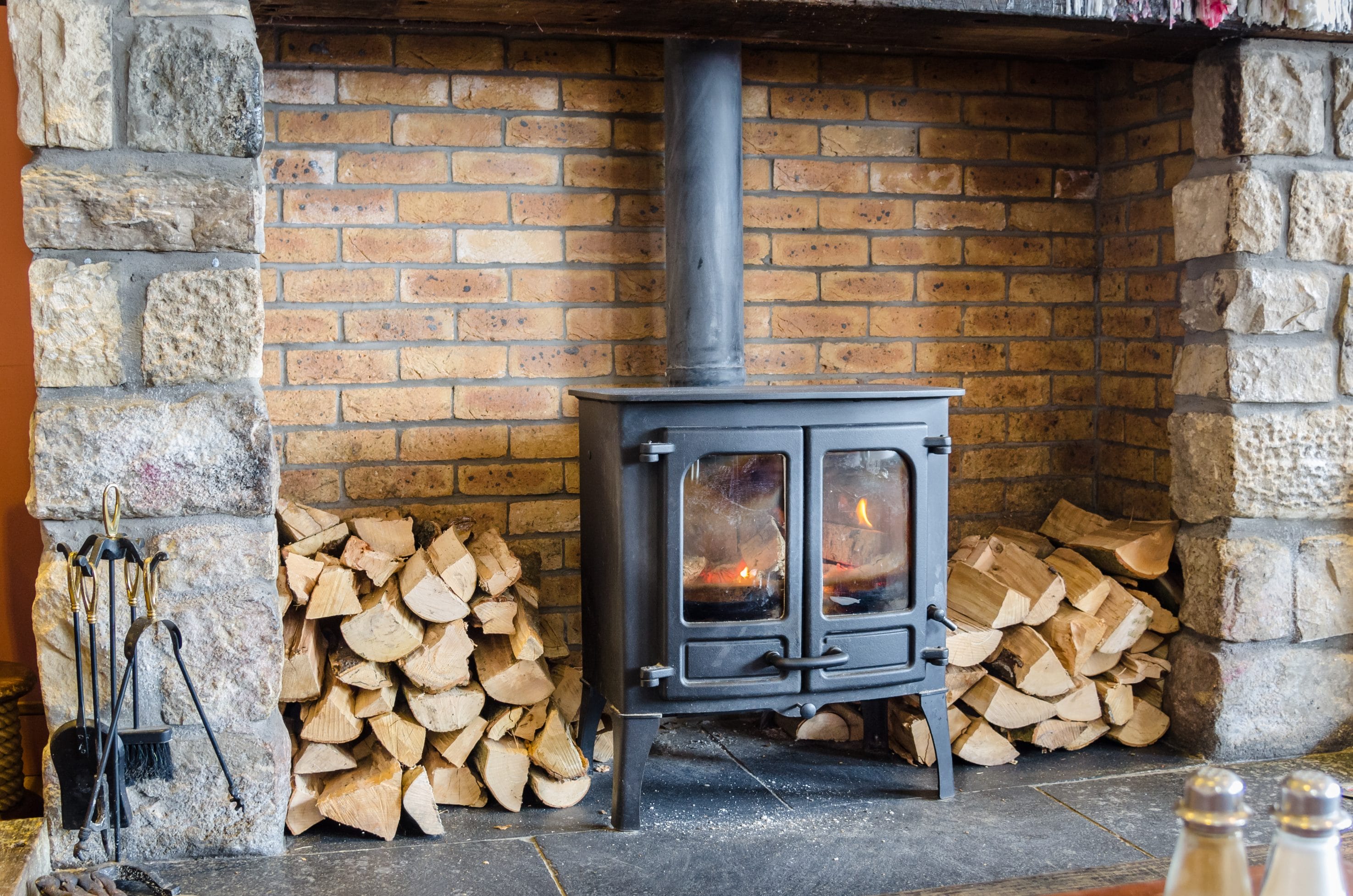 A stock image of a wood stove with wood log piles surrounding it.