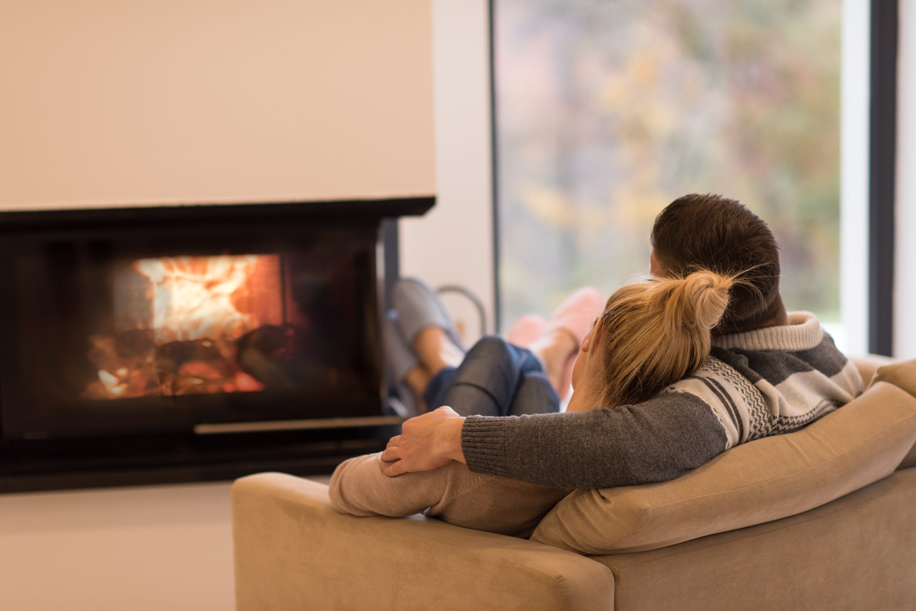 A stock image of a man and woman cuddling on a chair in front of a fireplace.