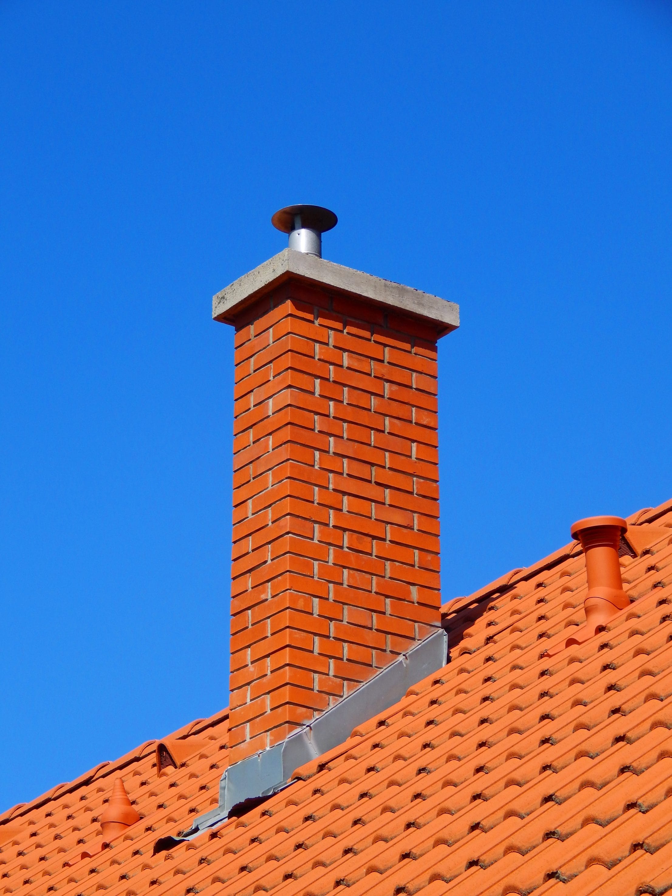 A stock image of well-cared for masonry chimney with metal flashing and a chimney cap.